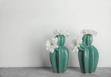 Trendy cactus shaped vases with flowers on table against light wall. Creative decor