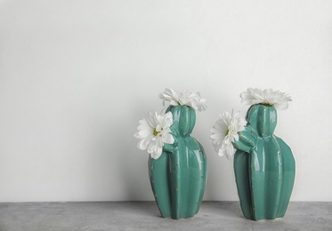 Photo of Trendy cactus shaped vases with flowers on table against light wall. Creative decor