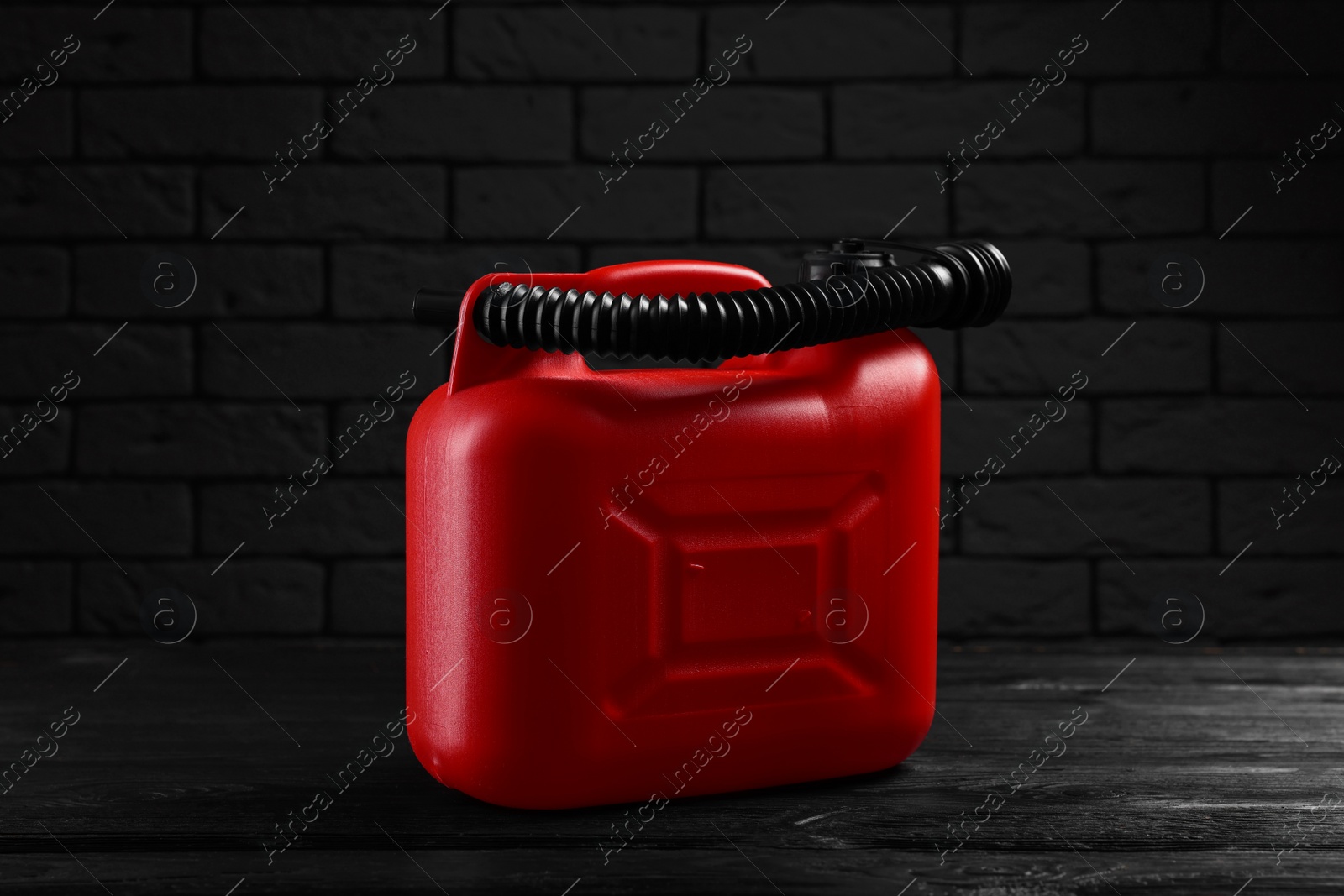 Photo of Red plastic canister on black wooden table against dark brick wall
