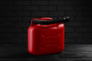 Red plastic canister on black wooden table against dark brick wall