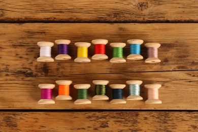 Photo of Different colorful sewing threads on wooden background, flat lay