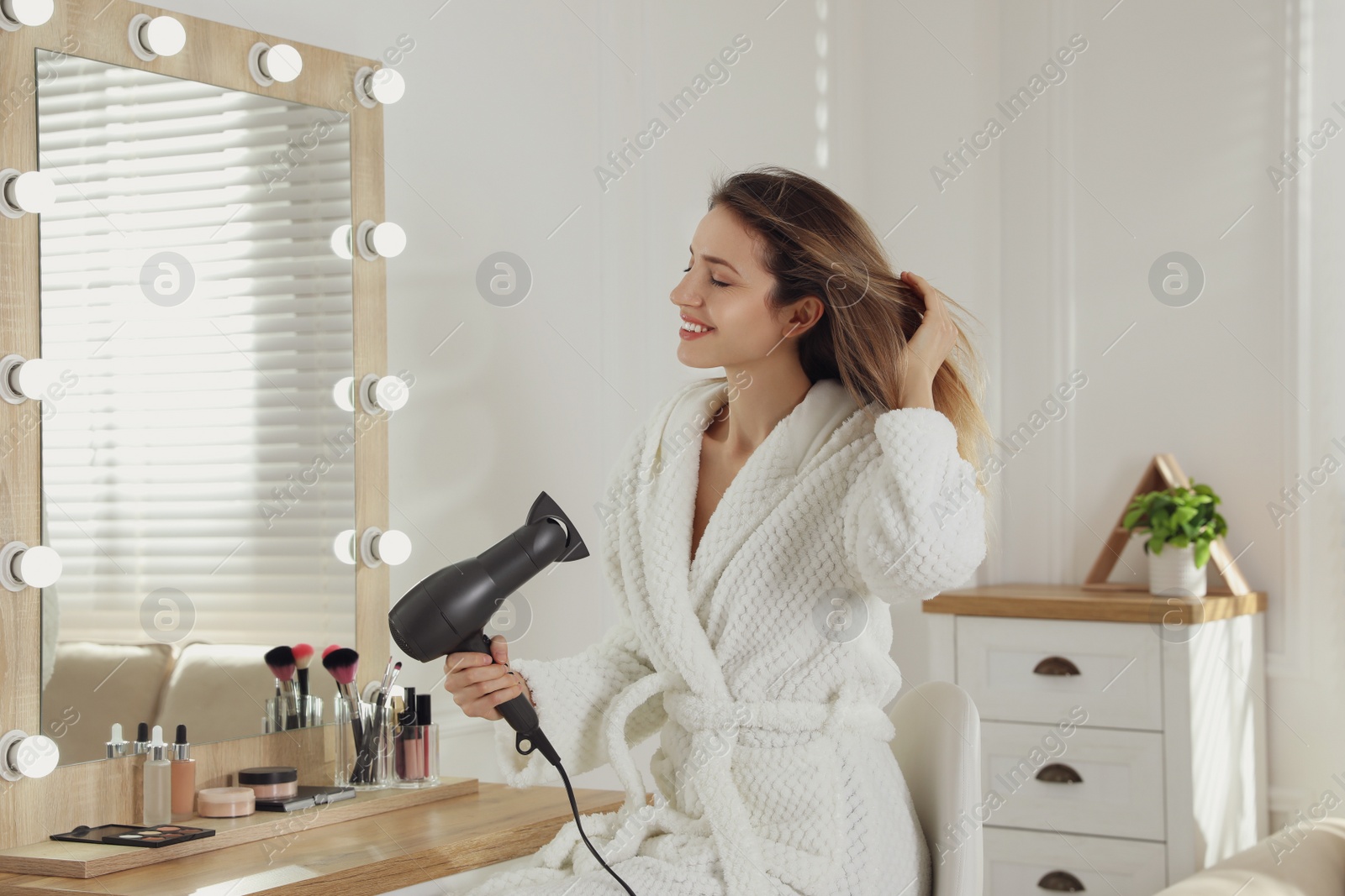 Photo of Beautiful young woman using hair dryer near mirror at home