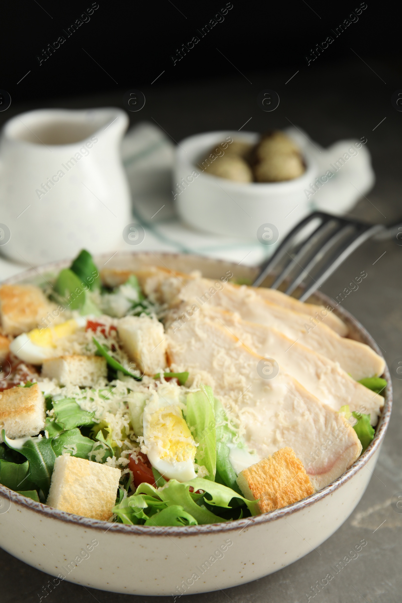 Photo of Delicious Caesar salad in bowl on grey table, closeup