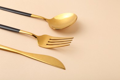 Photo of Stylish golden cutlery set on beige background, closeup. Space for text