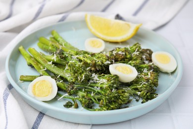 Tasty cooked broccolini with cheese, quail eggs and lemon on white table, closeup