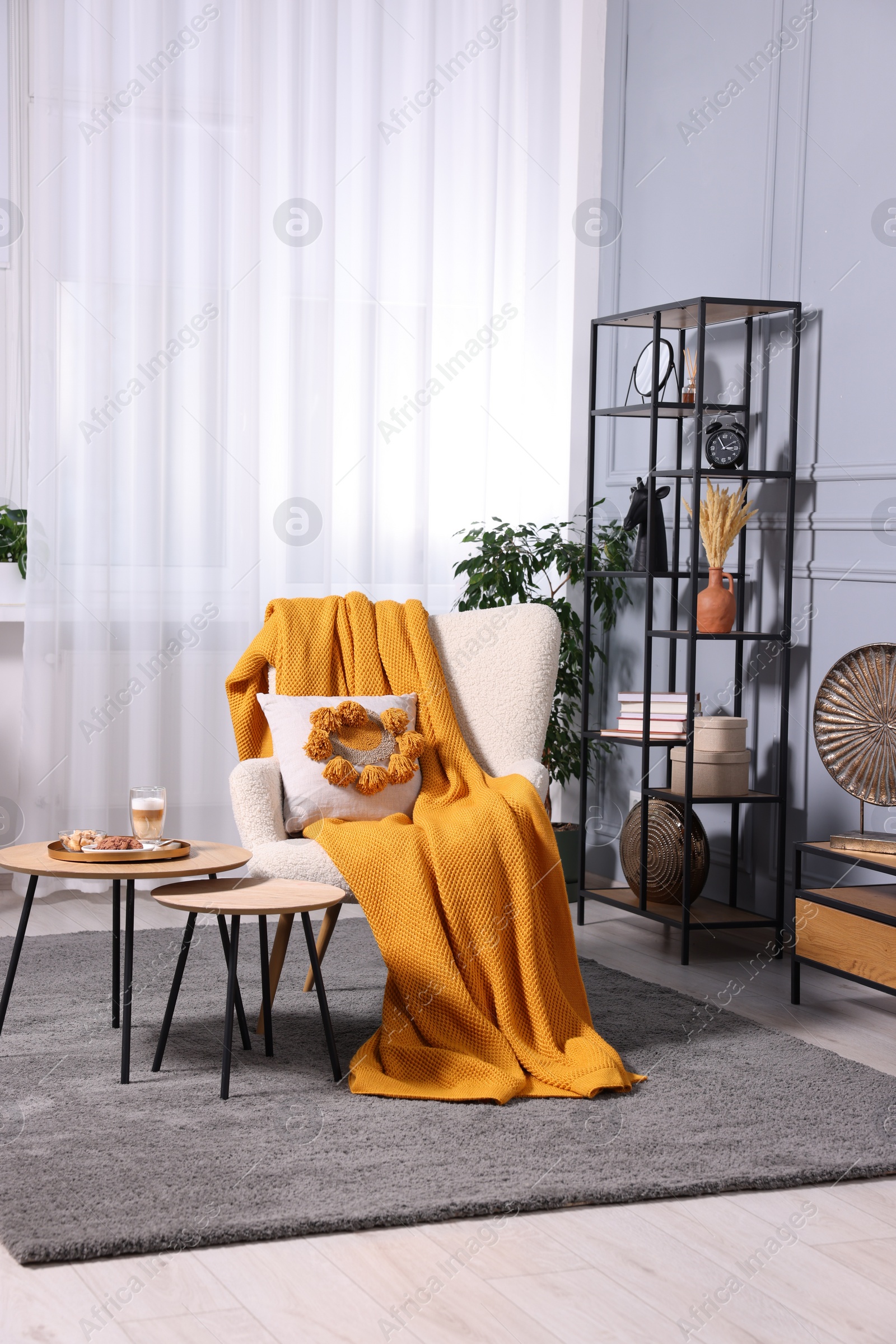 Photo of Stylish room interior with comfortable armchair, blanket and nesting tables