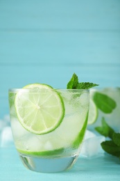 Photo of Glass of cocktail with vodka, ice and lime on blue wooden table