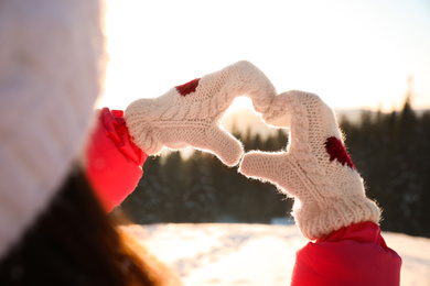 Woman making heart with hands outdoors, closeup. Winter vacation