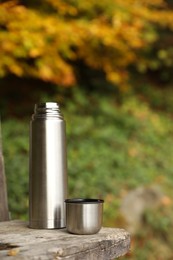 Photo of Metallic thermos and cup lid on wooden bench outdoors, space for text