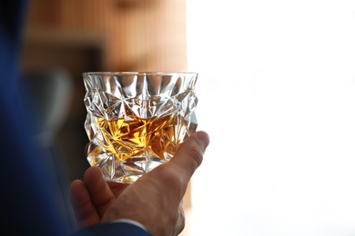 Young man with glass of whiskey indoors, closeup view. Space for text
