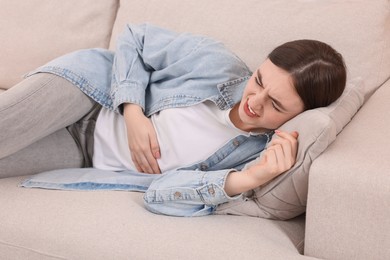 Photo of Young woman suffering from stomach pain on sofa