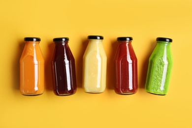 Bottles with delicious colorful juices on yellow background, flat lay