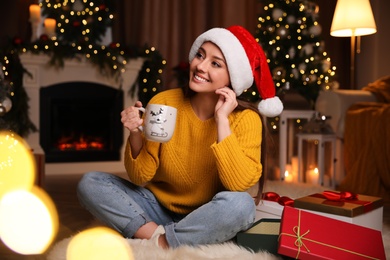 Beautiful young woman with cup of hot drink in living room decorated for Christmas