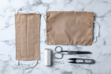 Photo of Homemade protective masks and sewing accessories on white marble background, flat lay