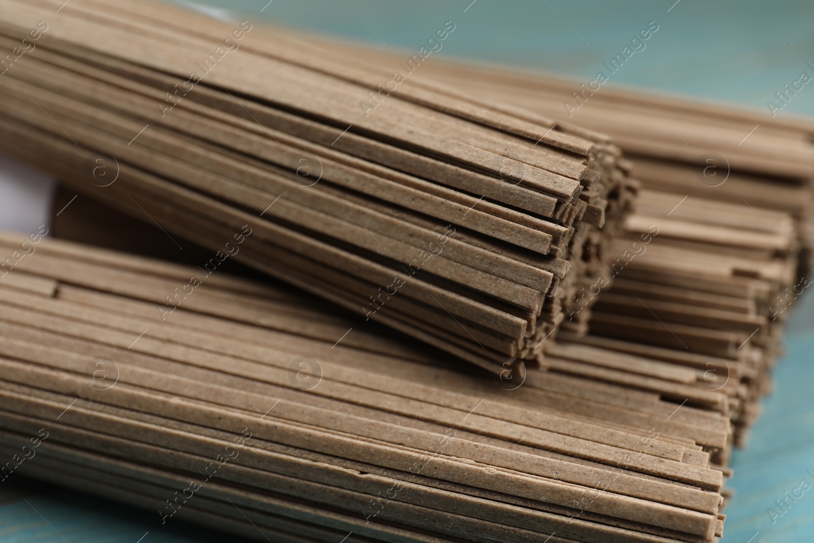 Photo of Uncooked buckwheat noodles (soba) on light blue wooden table, closeup