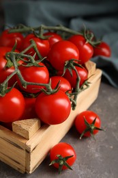 Photo of Many ripe red tomatoes in wooden crate on grey table, closeup