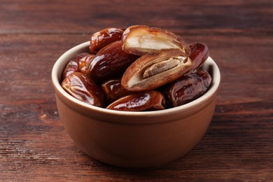 Photo of Sweet dried dates in bowl on wooden table, closeup