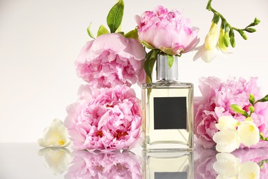 Photo of Bottle of luxury perfume and floral decor on mirror surface against white background