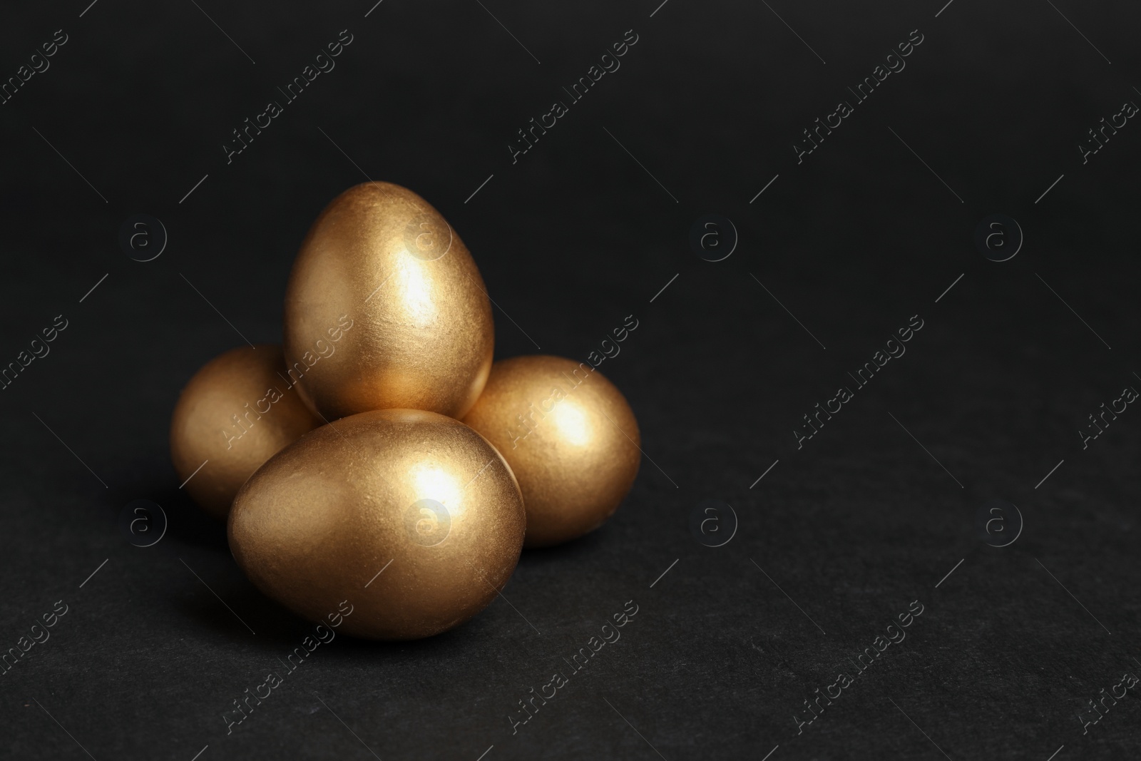 Photo of Shiny golden eggs on black background, space for text