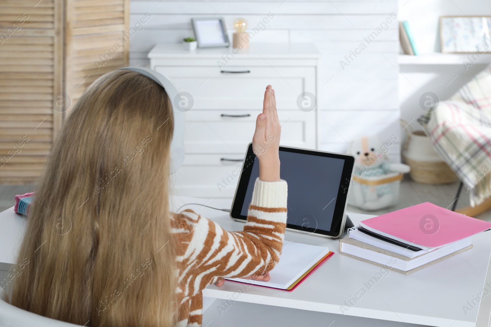 Photo of Cute little girl with modern tablet studying online at home, back view. E-learning