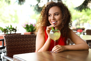 Photo of Happy African-American woman with glass of natural lemonade in cafe. Detox drink