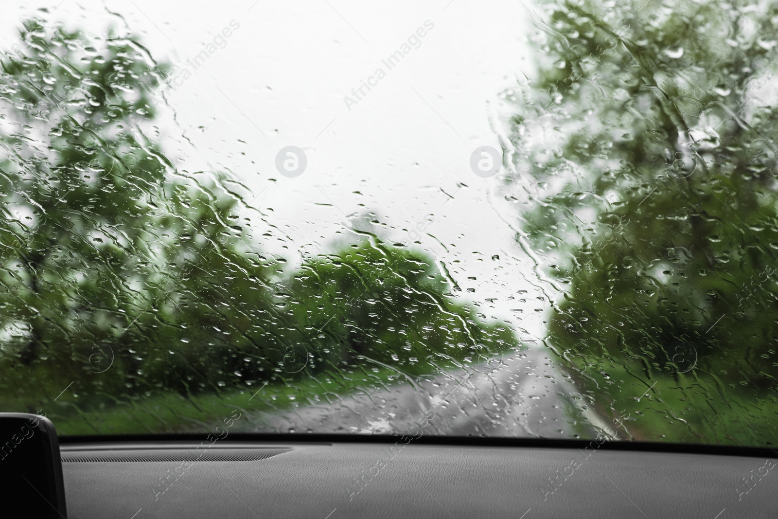 Photo of Blurred view of suburban road through wet car window. Rainy weather