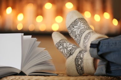 Photo of Woman wearing woolen socks relaxing on pouf against blurred background, closeup. Winter atmosphere