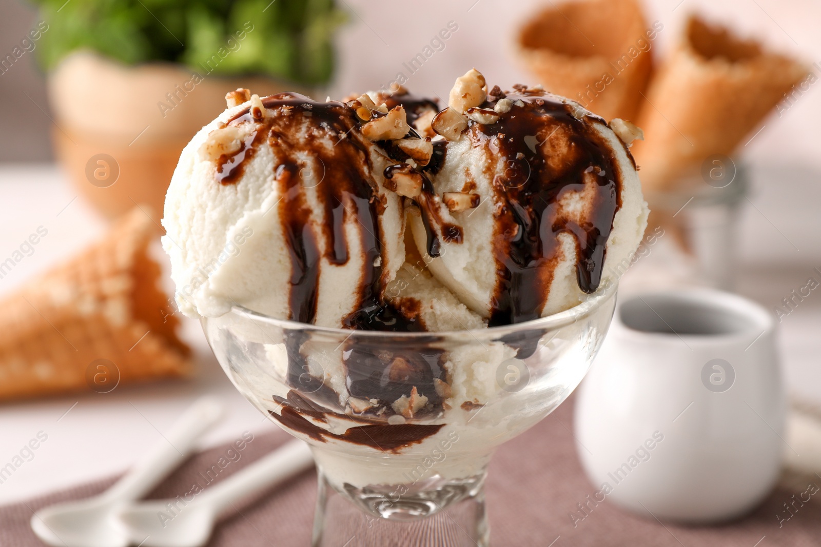 Photo of Tasty ice cream with chocolate topping and nuts in glass dessert bowl on table, closeup