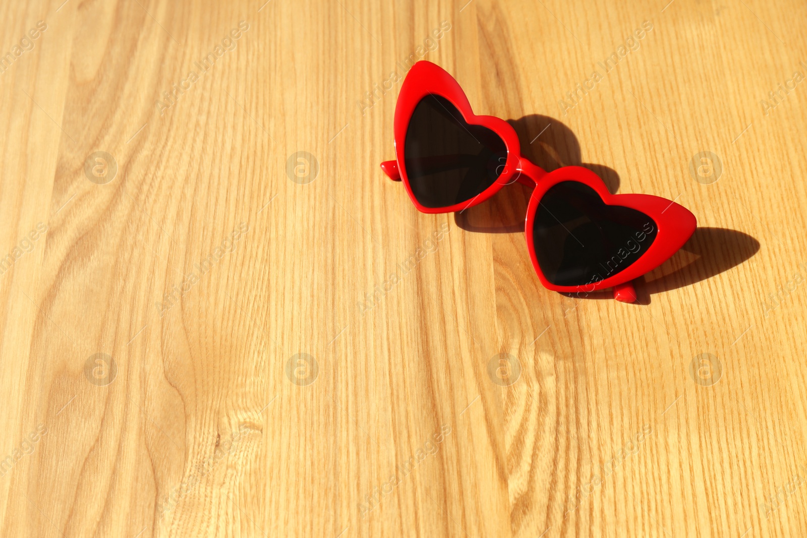 Photo of Stylish heart shaped sunglasses on wooden background, space for text