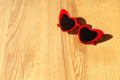 Stylish heart shaped sunglasses on wooden background, space for text