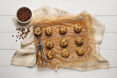 Photo of Uncooked chocolate chip cookies and scoop on white wooden table, flat lay