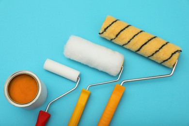 Can of orange paint and rollers on turquoise background, flat lay
