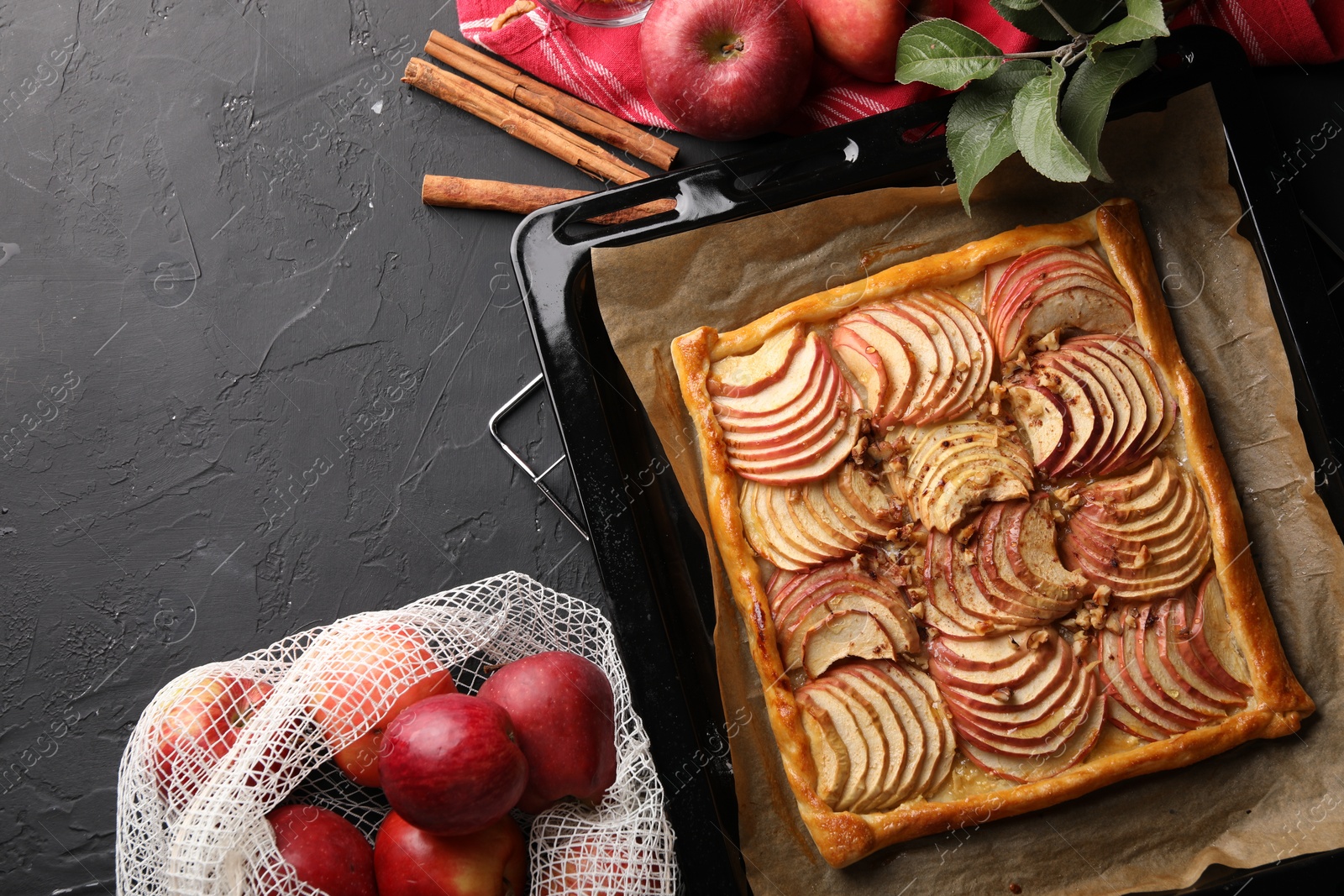 Photo of Baking tray with fresh apple galette and fruits on black table, flat lay. Space for text