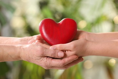 Photo of Young and elderly women holding red heart in hands on blurred green background, closeup