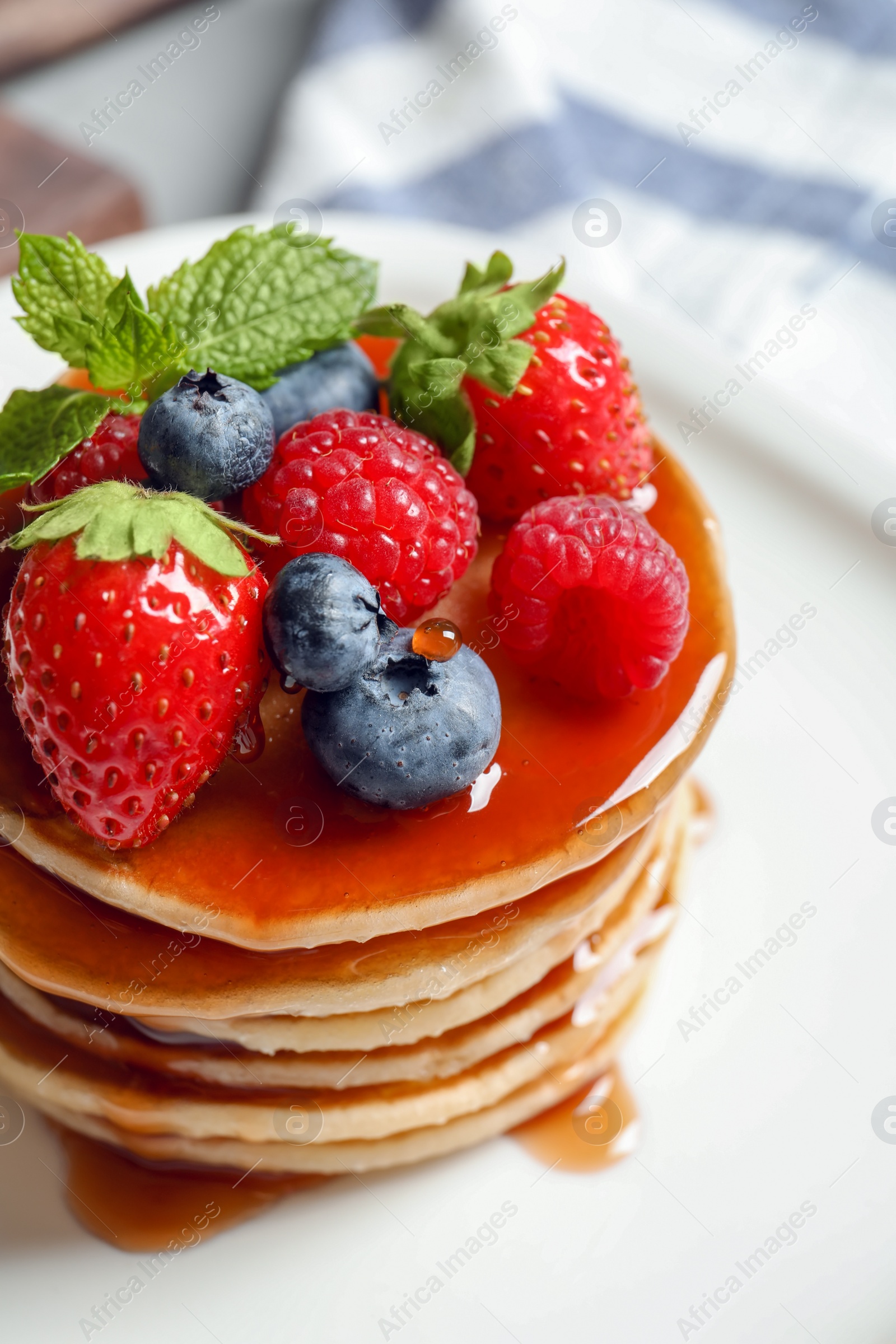 Photo of Tasty pancakes with berries and syrup on plate, closeup