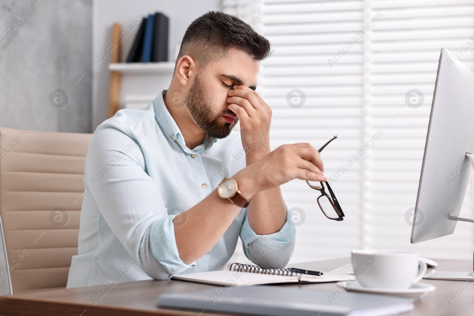 Photo of Overwhelmed man with glasses sitting at table in office