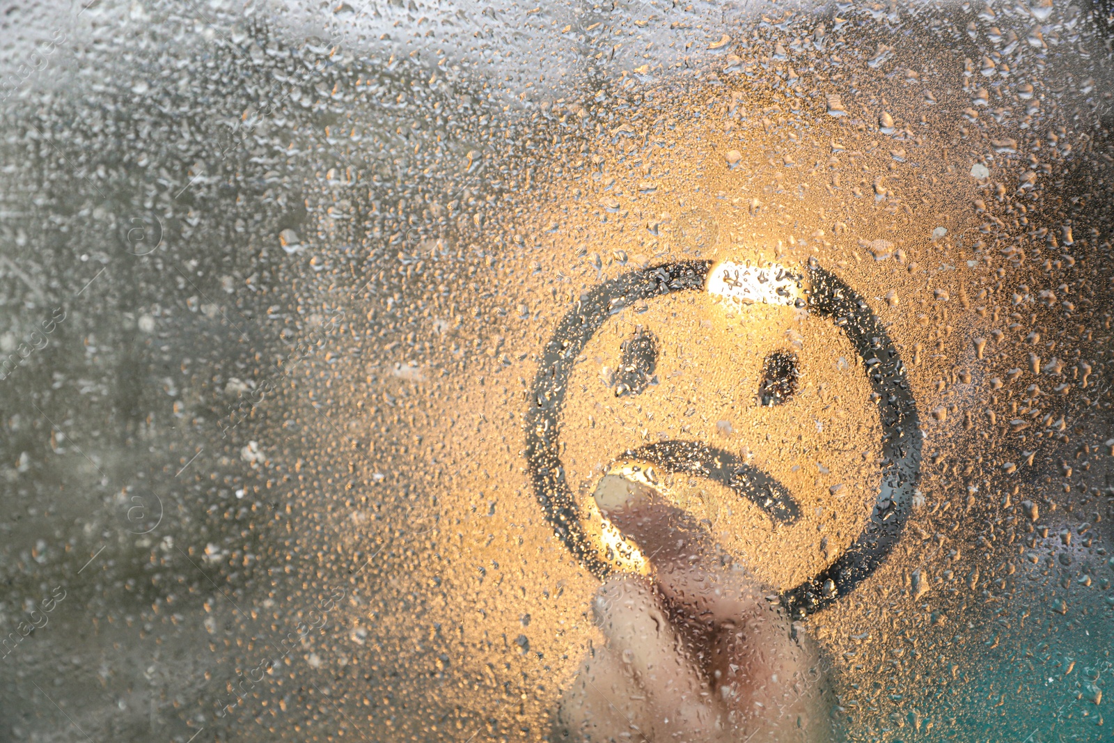 Photo of Woman drawing sad face on foggy window at rainy weather