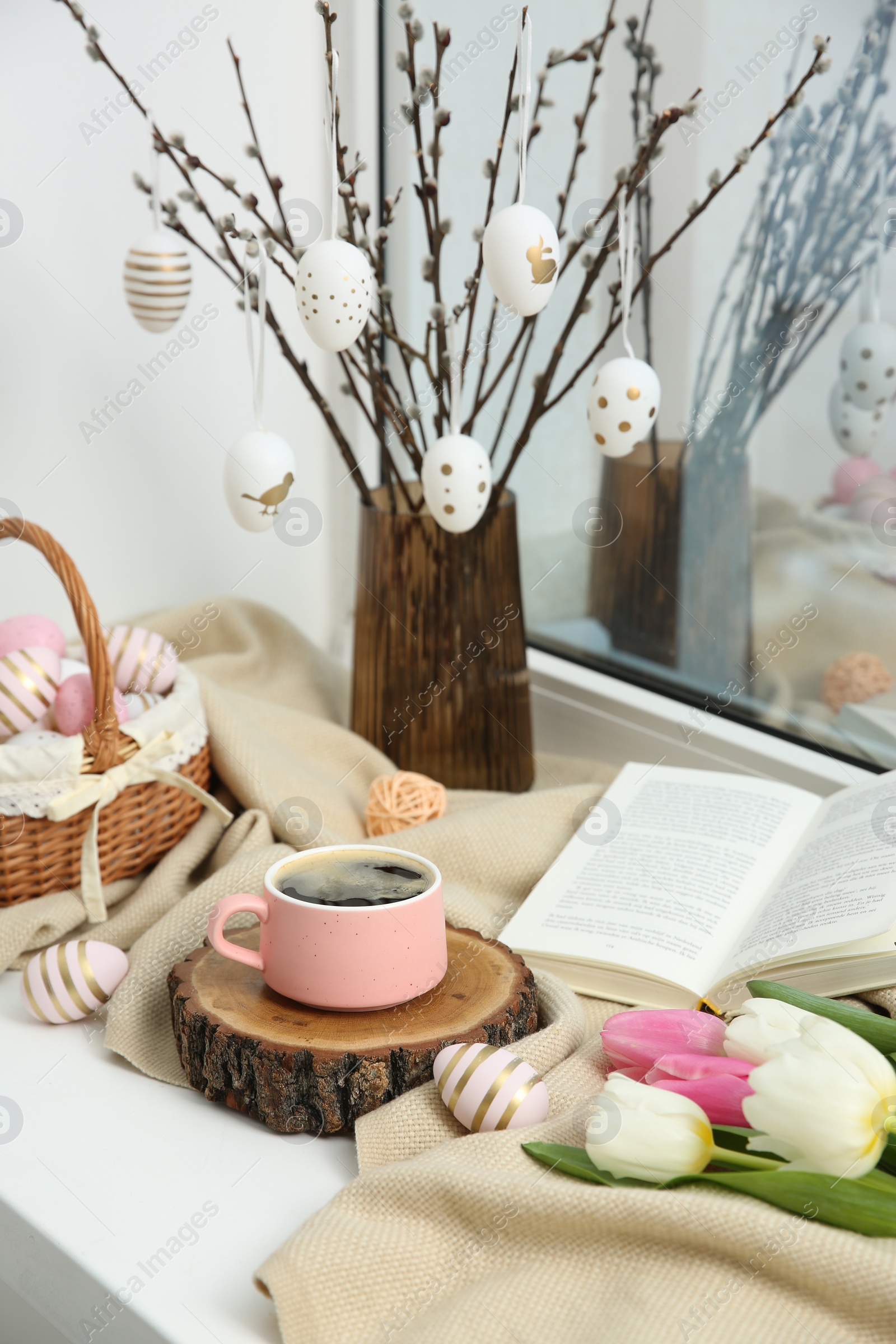 Photo of Easter decorations. Cup of coffee, painted eggs, tulips and book on windowsill