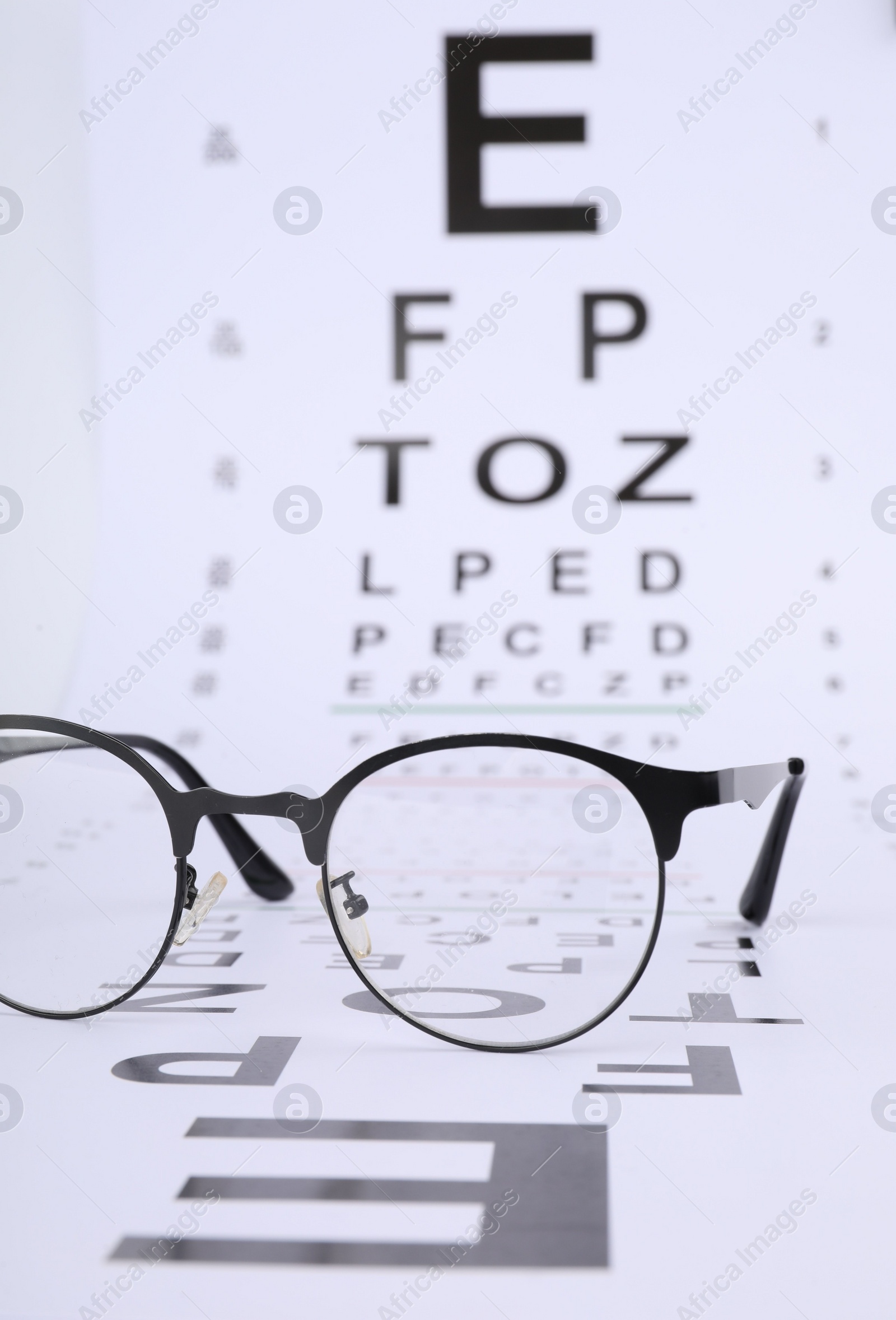 Photo of Vision test chart and glasses on white background, closeup