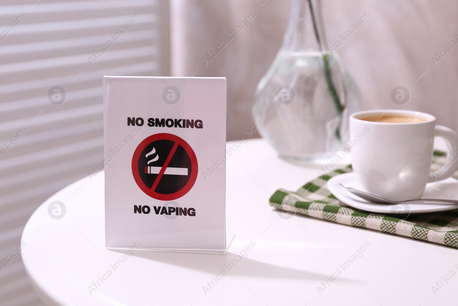 Photo of No Smoking No Vaping sign and cup of coffee on white table indoors