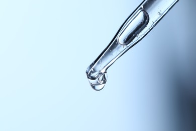 Dripping liquid from pipette on light blue background, closeup