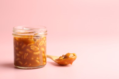 Photo of Tasty salted caramel with peanuts on pink background, space for text