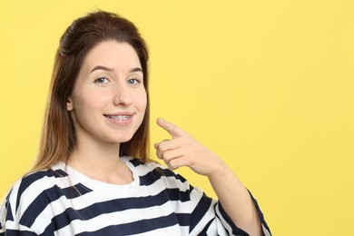 Photo of Smiling woman pointing at her dental braces on yellow background, closeup. Space for text
