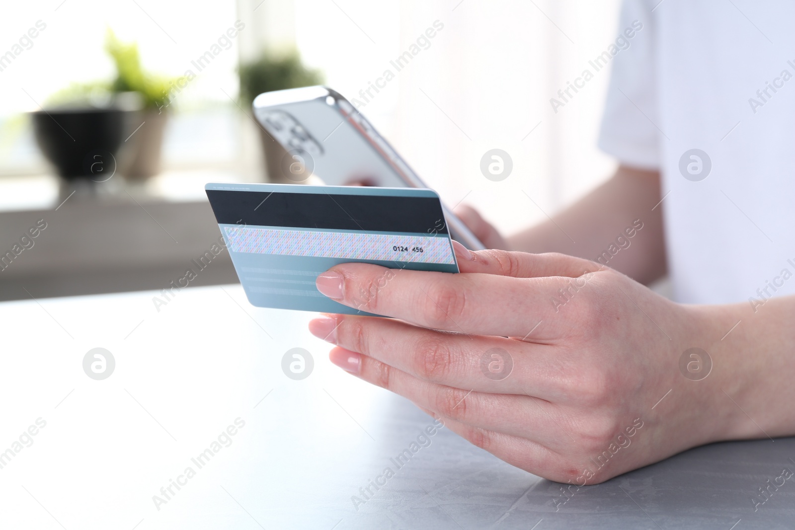 Photo of Online payment. Woman with smartphone and credit card at white table, closeup