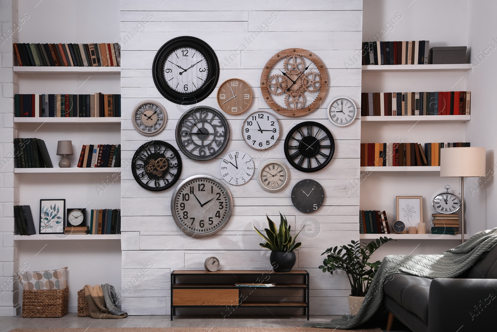 Photo of Stylish room interior with console table, comfortable sofa and collection of different clocks on white wall