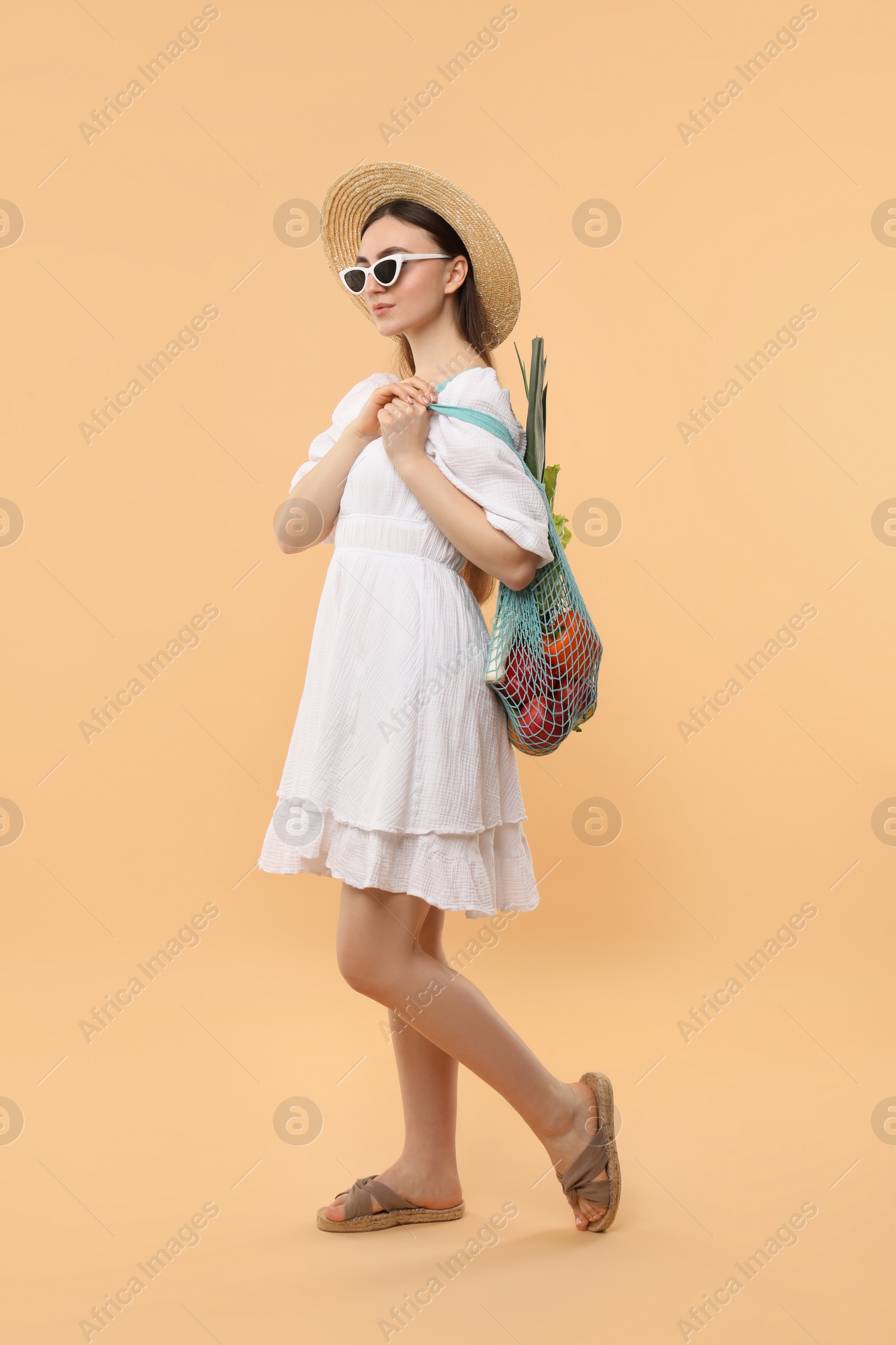 Photo of Woman with string bag of fresh vegetables on beige background