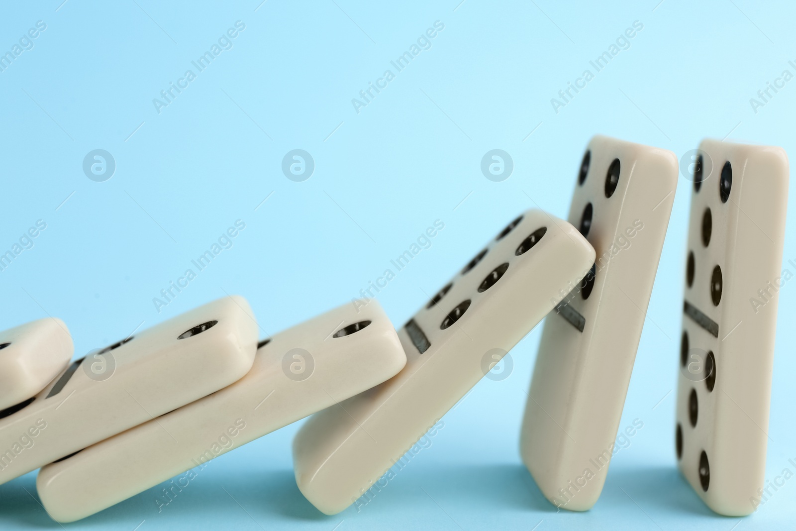 Photo of White domino tiles falling on light blue background, closeup. Space for text