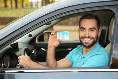 Photo of Young man holding driving license in car