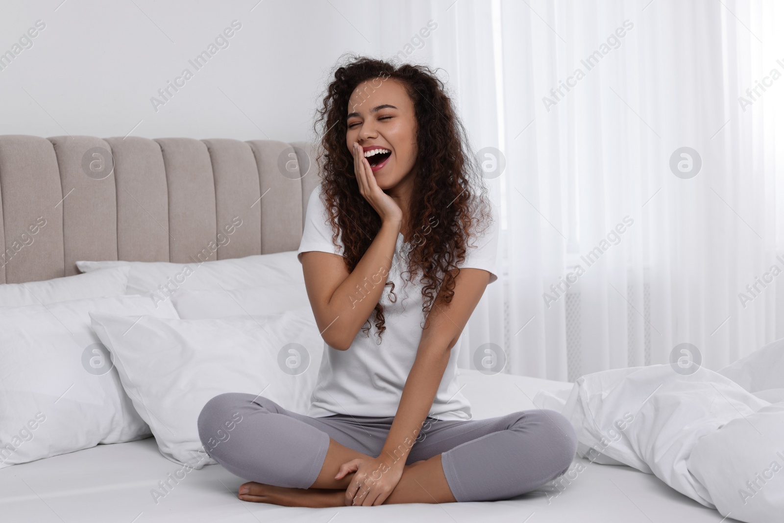 Photo of Happy African American woman yawning on bed at home