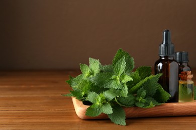 Photo of Tray with bottles of nettle oil and fresh leaves on wooden table against brown background, space for text